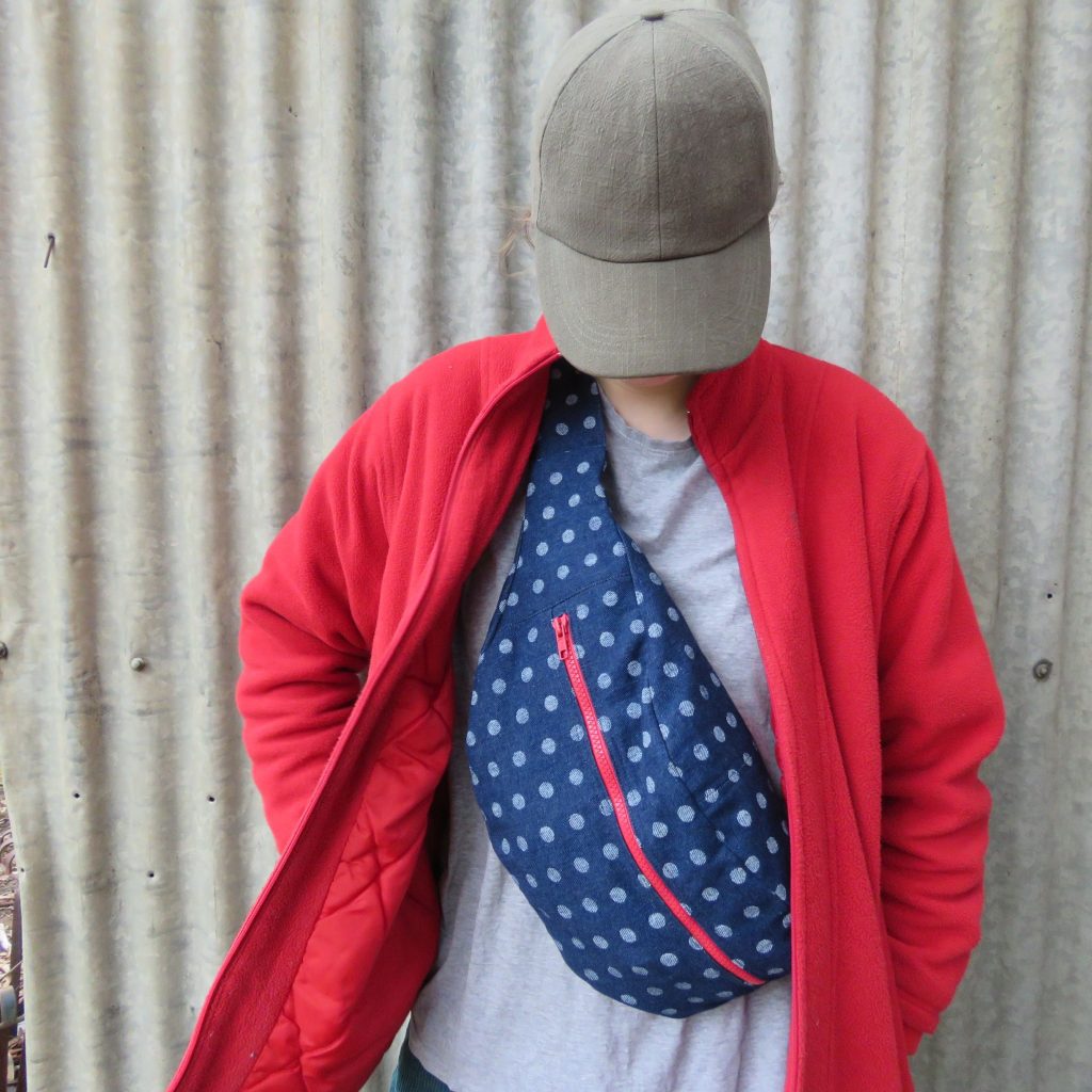 Zero waste cross body bag worn with grey t-shirt and red jacket.